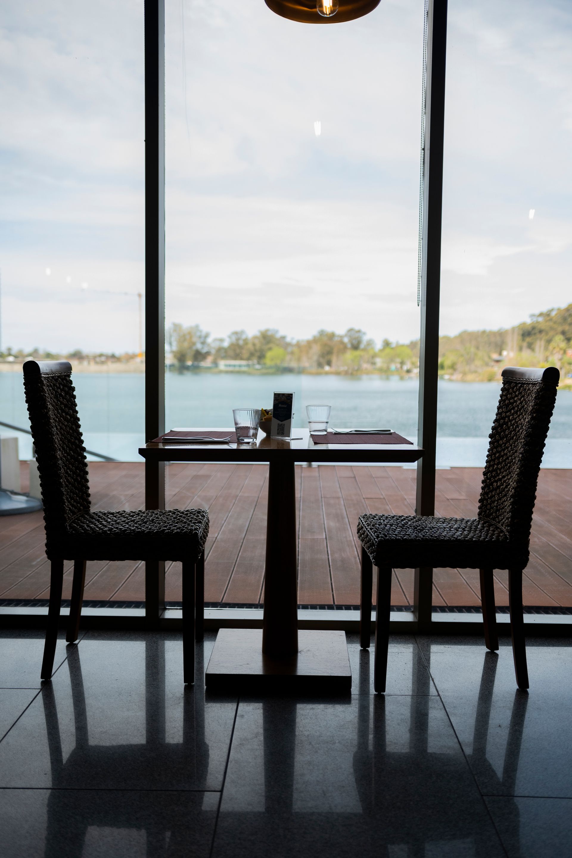 Dos sillas y una mesa frente a una ventana con vista a un lago.