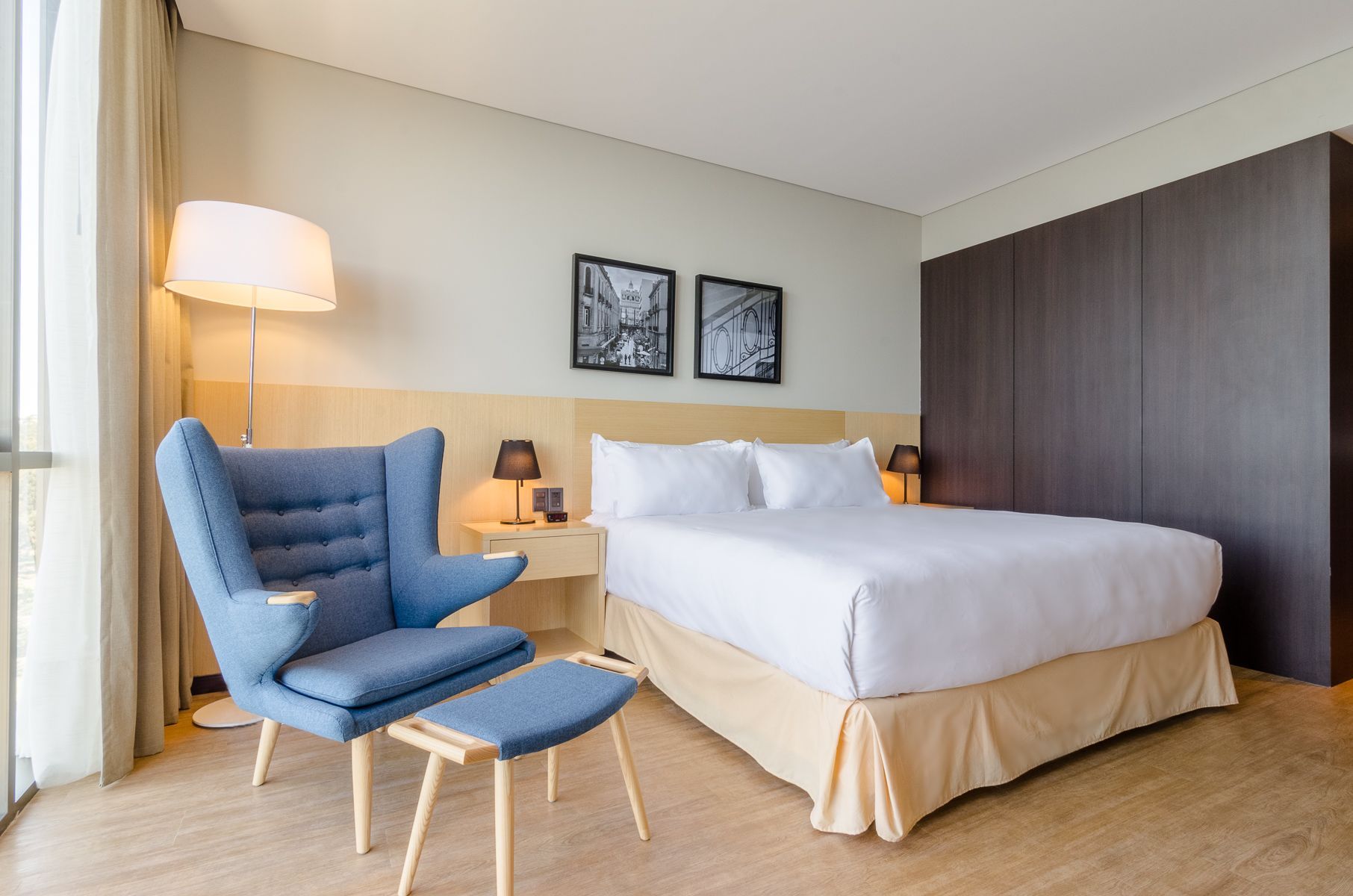 Una habitación de hotel con cama, silla, lámpara y ventana.