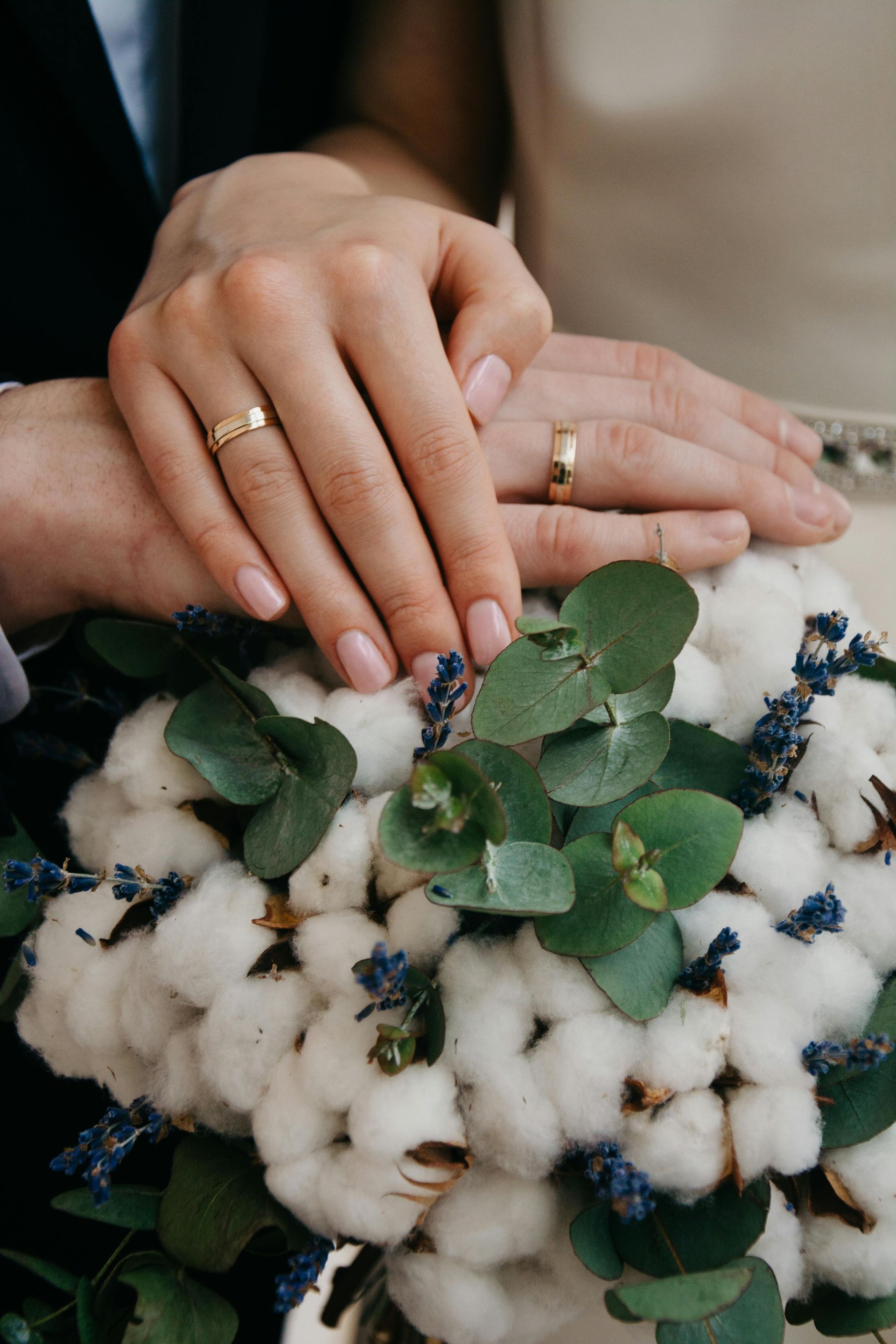 Una novia y un novio están tomados de la mano sobre un ramo de flores de algodón.