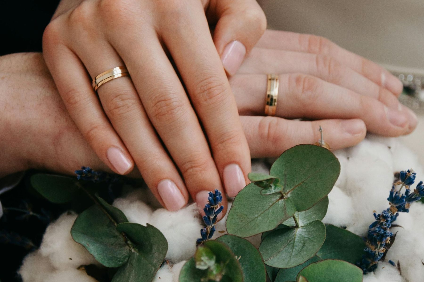 Un hombre y una mujer están tomados de la mano con anillos de boda en los dedos.