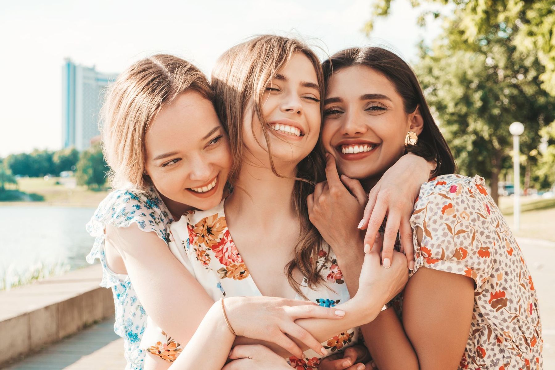 Tres mujeres jóvenes se abrazan y sonríen en un parque.