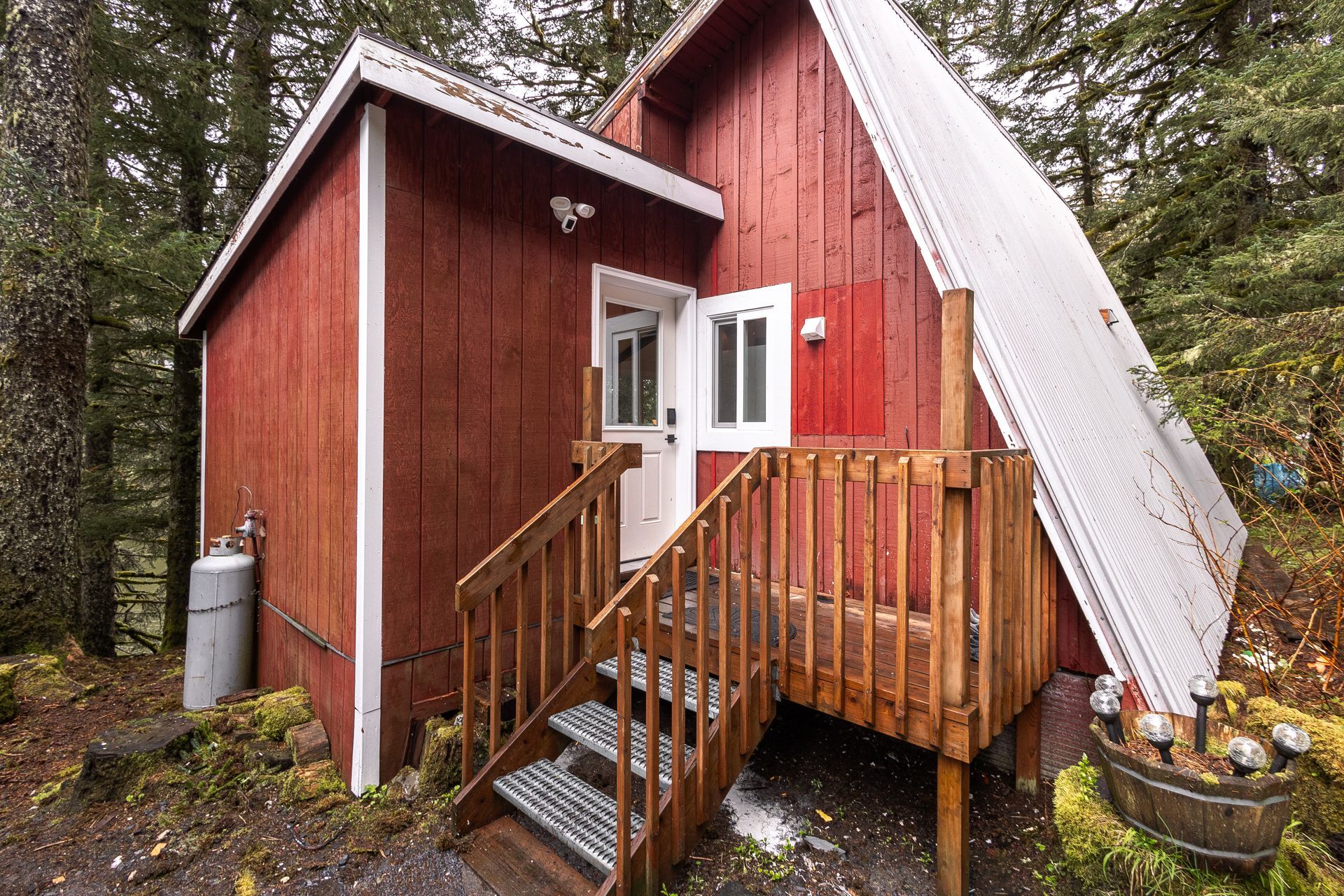 Red wooden cabin with a small porch and white tarp covering one side in a wooded area
