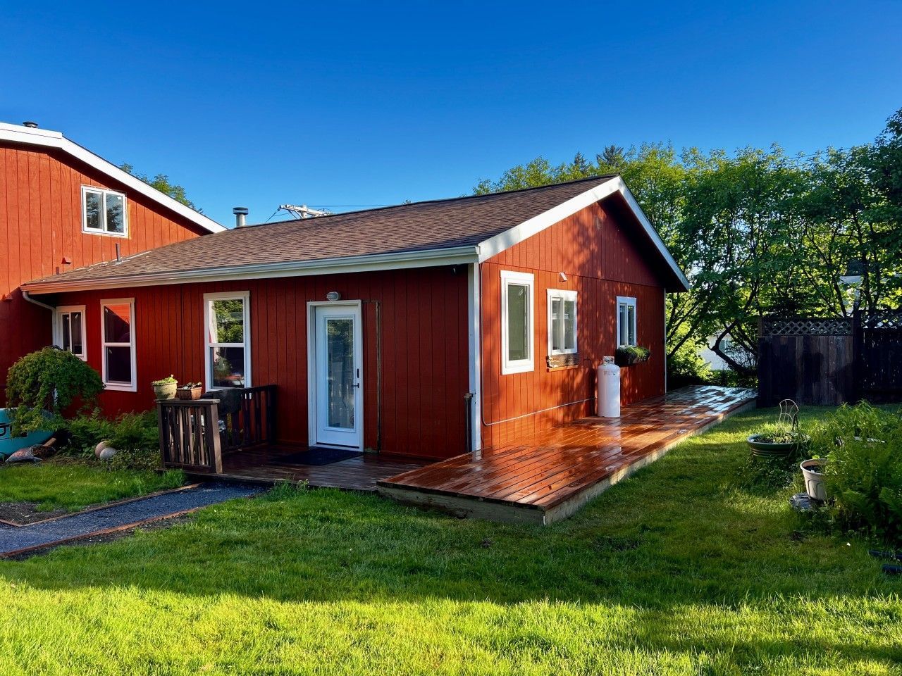 Red wooden cottage with white trim and a small porch in a sunny green yard
