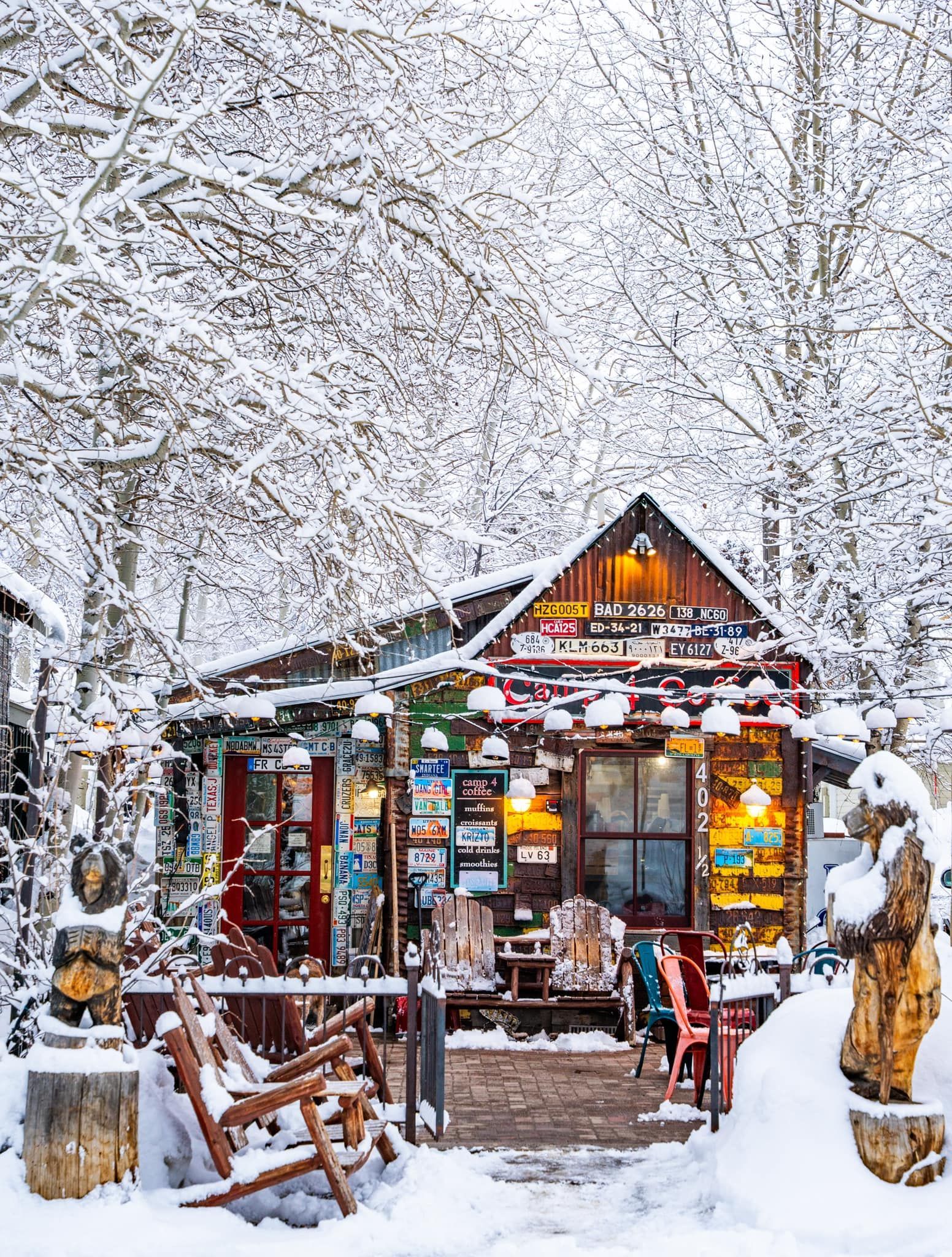 Snow-covered rustic cabin with colorful lights and benches in a winter forest scene