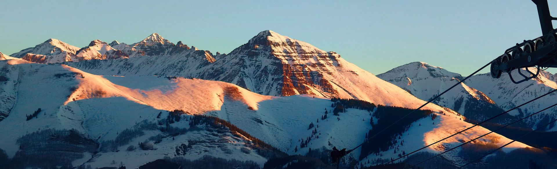 Snowy mountain peaks lit by warm sunlight under a clear blue sky