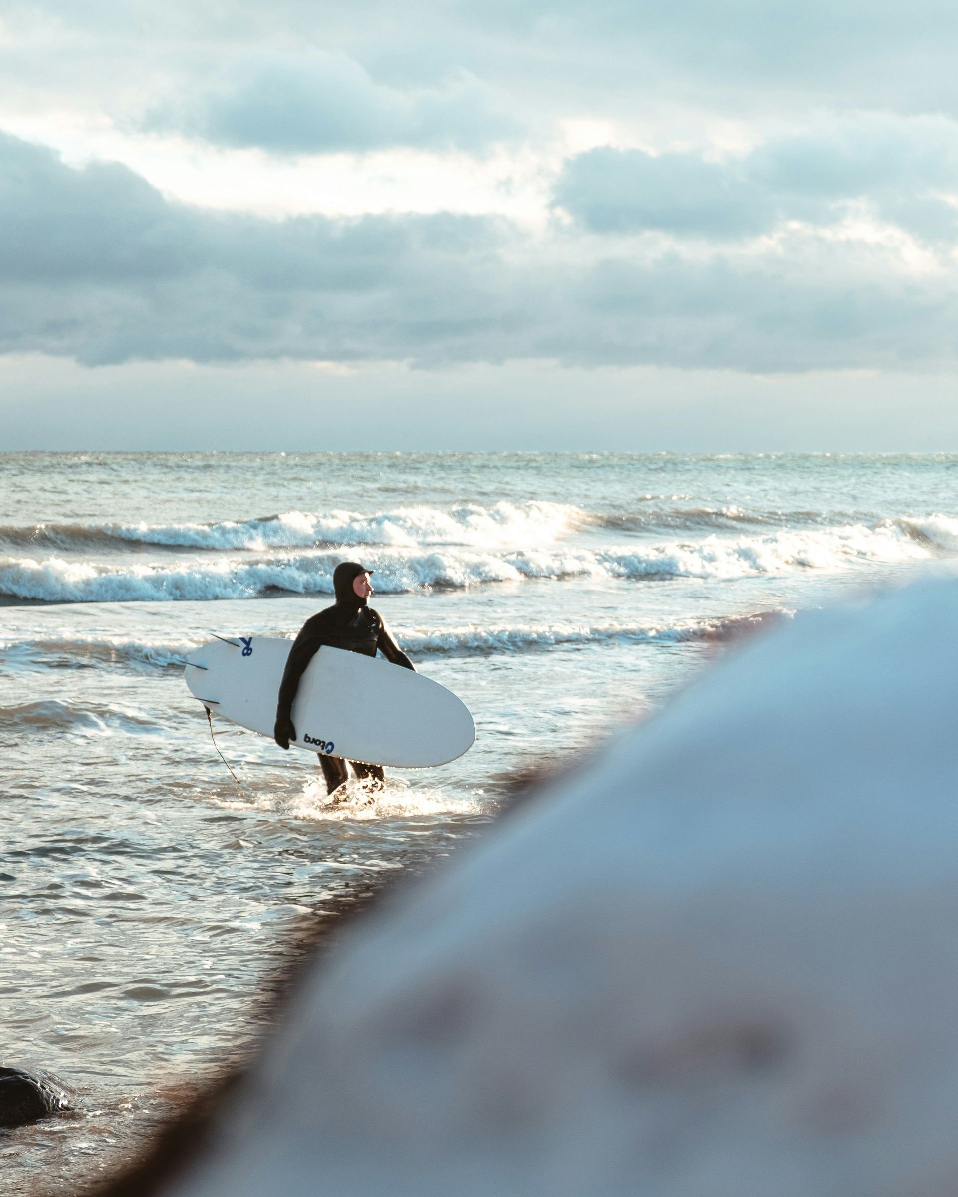 Surfer carrying a white board toward waves on a cloudy beach