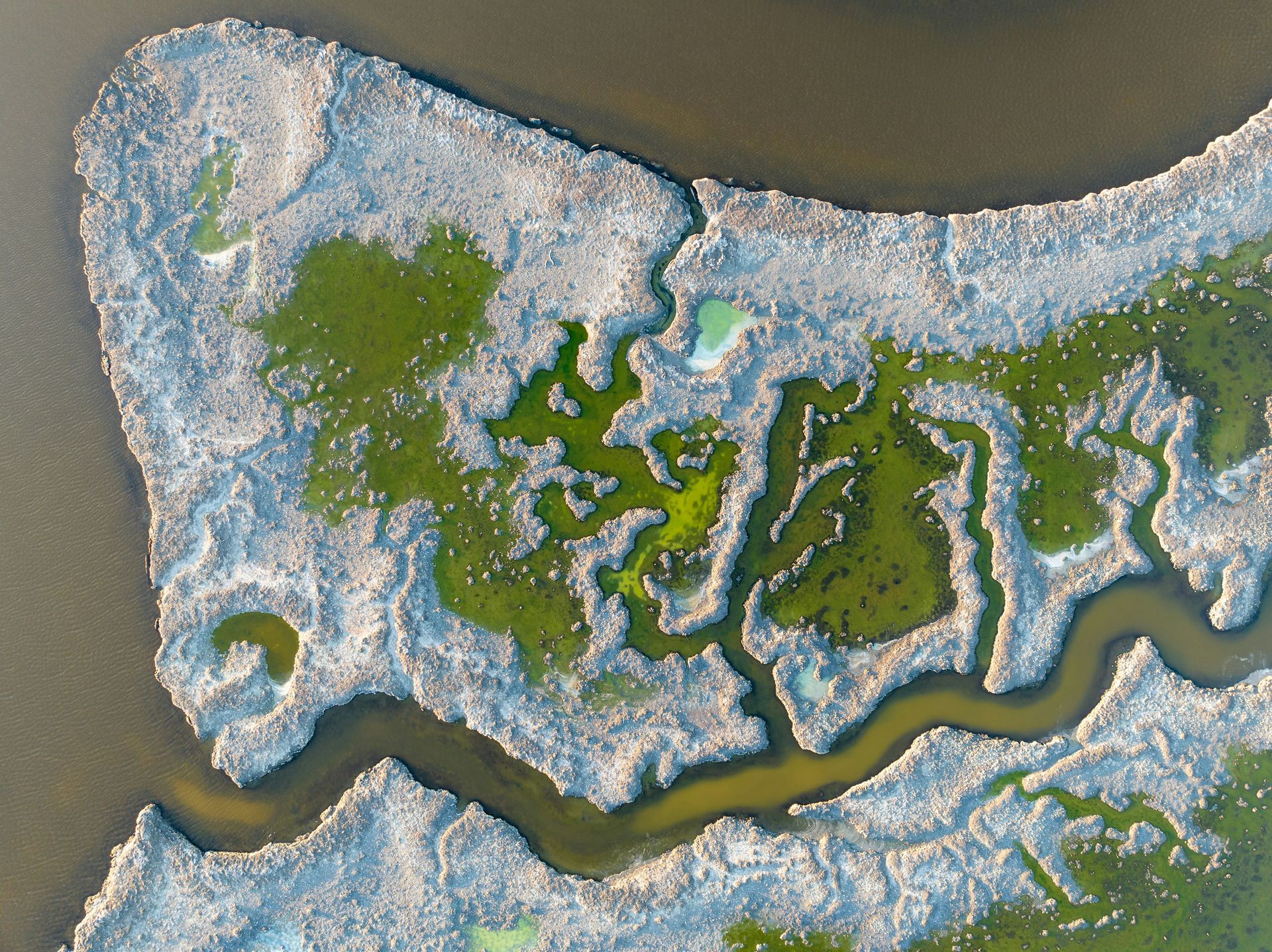 Aerial view of a winding river through snowy wetlands and green marsh islands