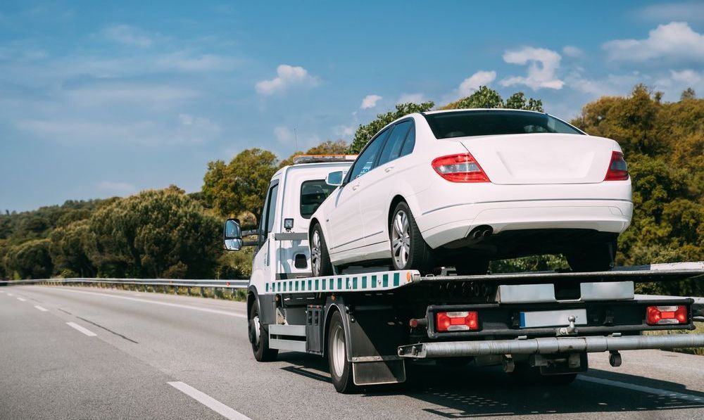A white car is being towed by a tow truck on a highway.