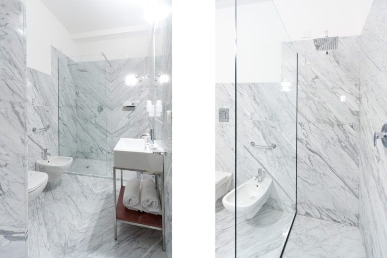 Un bagno moderno in marmo bianco con cabina doccia in vetro, lavabo a colonna e bidet.