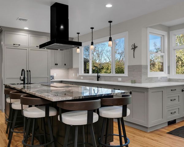 Modern white kitchen with black island, bar stools, and large windows overlooking trees