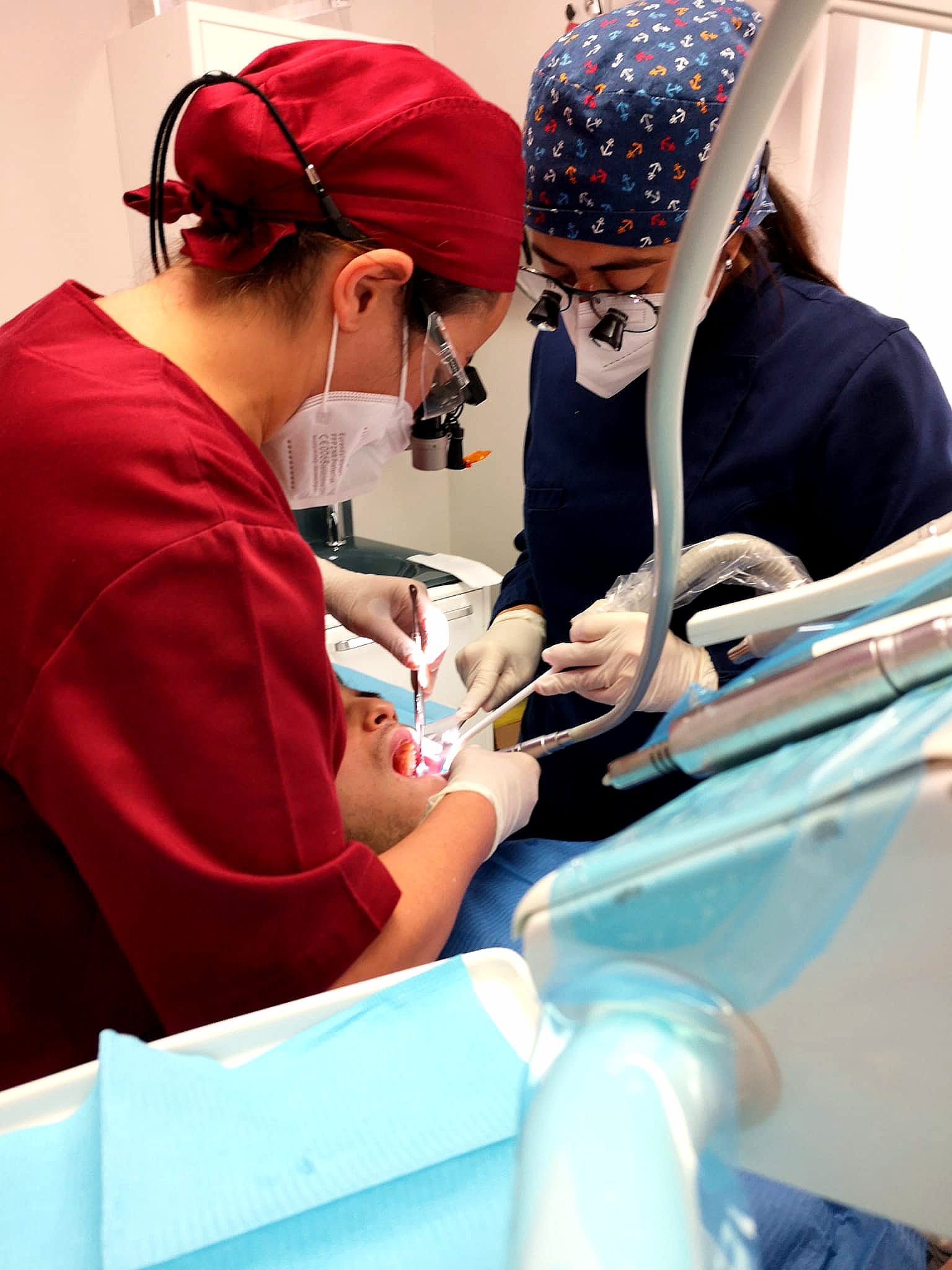 Due dentisti lavorano su un paziente in uno studio dentistico. Entrambi indossano mascherine e camici.