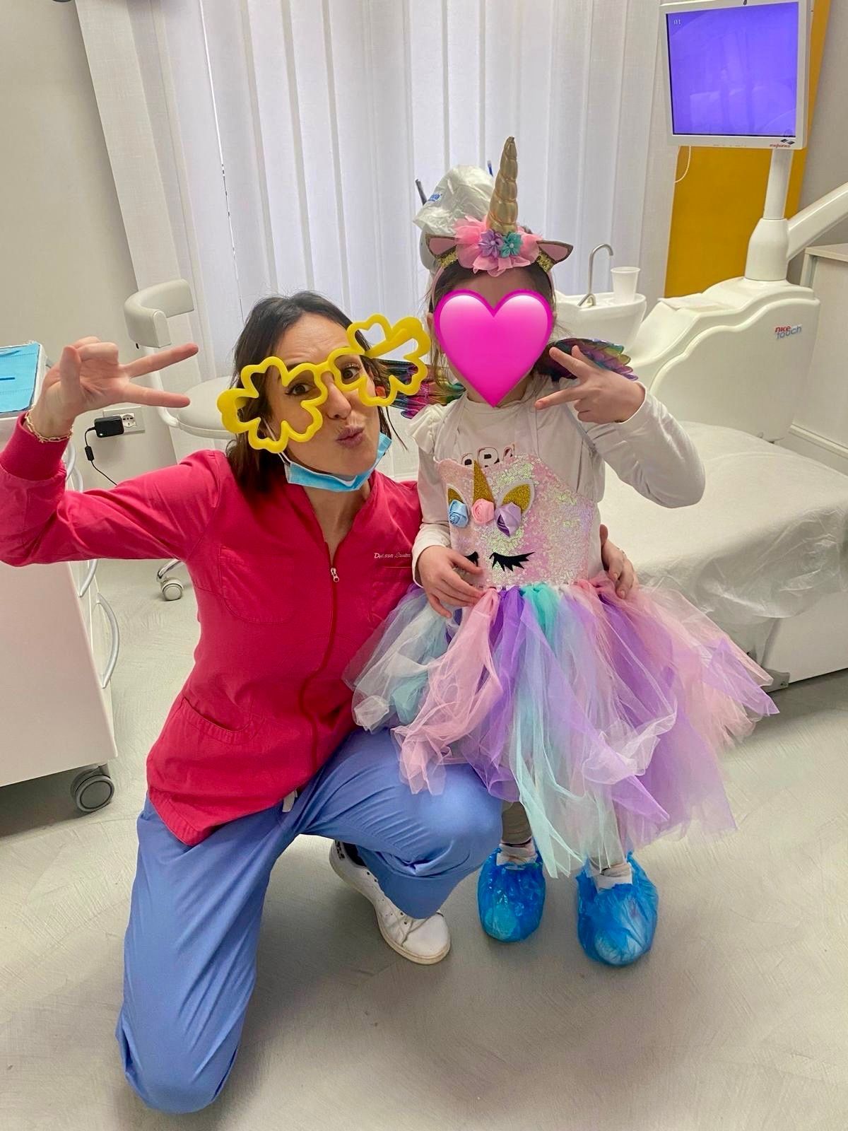 Il dentista e il bambino in costume da unicorno posano nello studio dentistico, entrambi facendo il segno della pace.