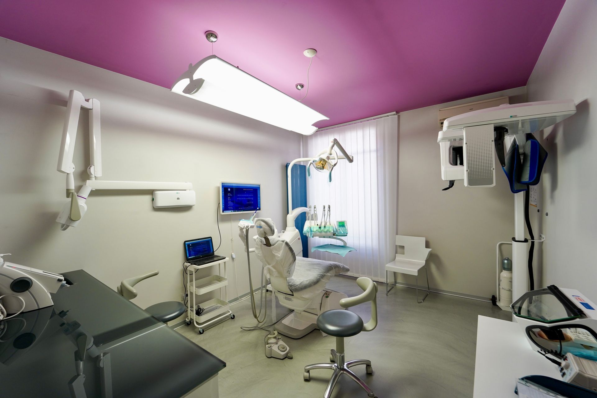 Studio dentistico con poltrona, strumenti e soffitto rosa.