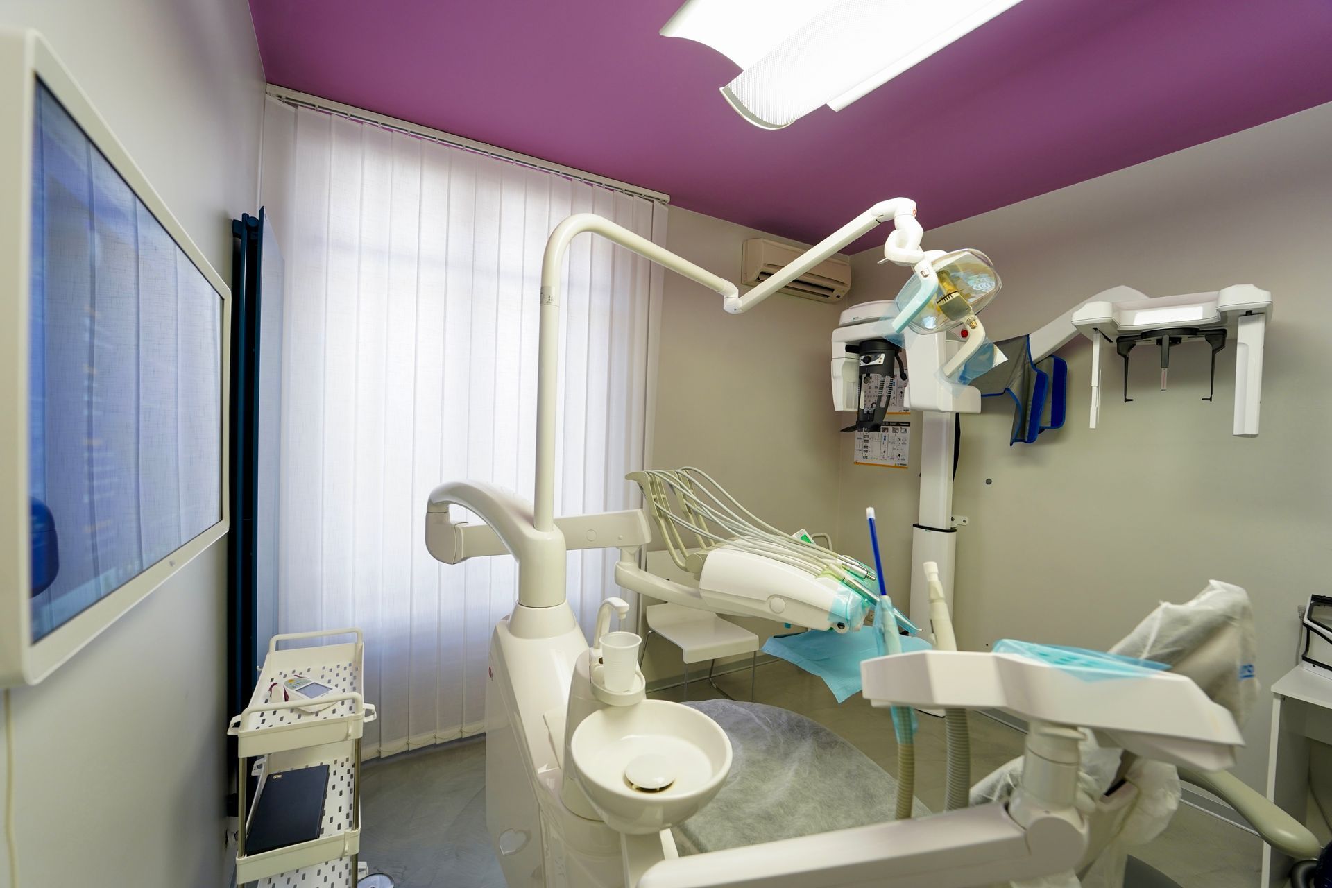 Sala visite dello studio dentistico con poltrona, attrezzatura e soffitto rosa.