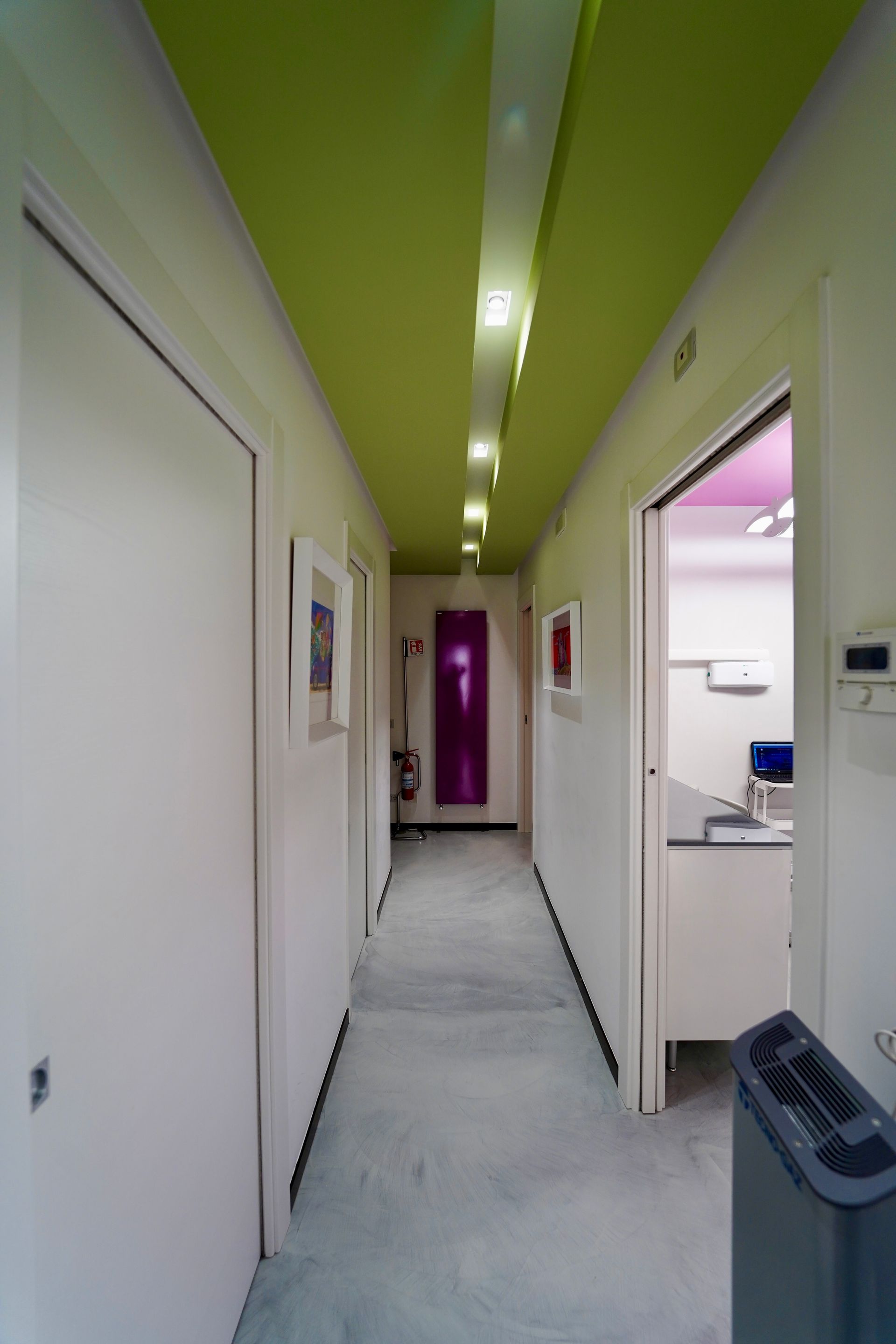 Corridoio con soffitto verde, pareti bianche e porte chiuse. Una porta è aperta e mostra le scale.