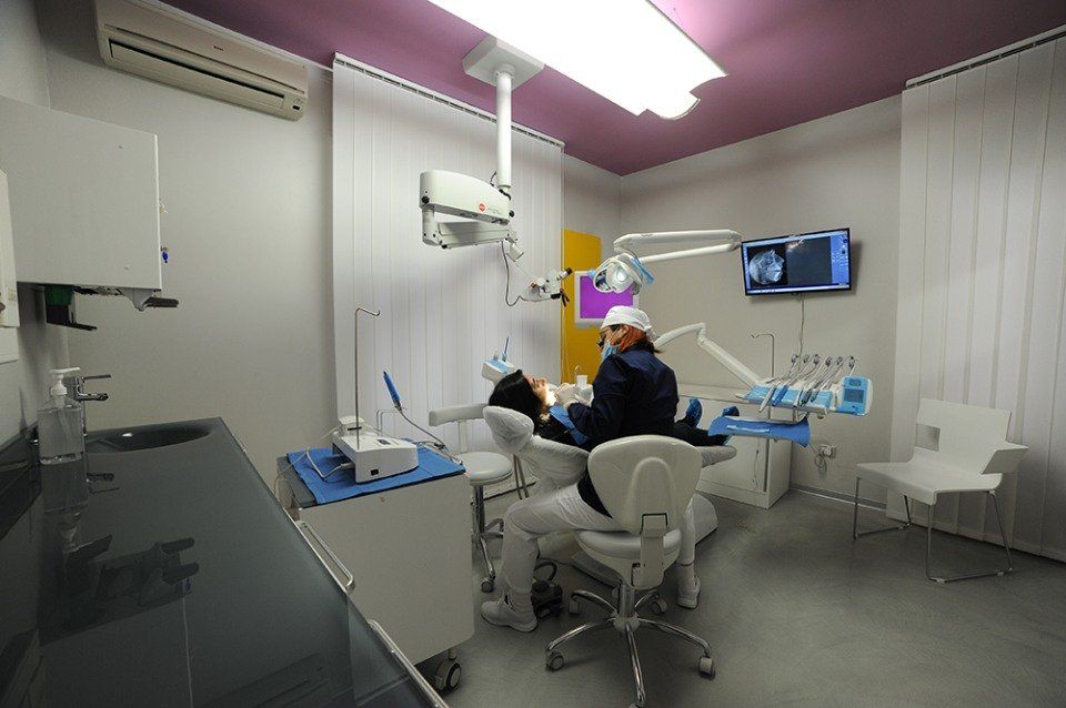 Un dentista visita un paziente in uno studio dentistico. La stanza è dotata di poltrona, strumenti e monitor.
