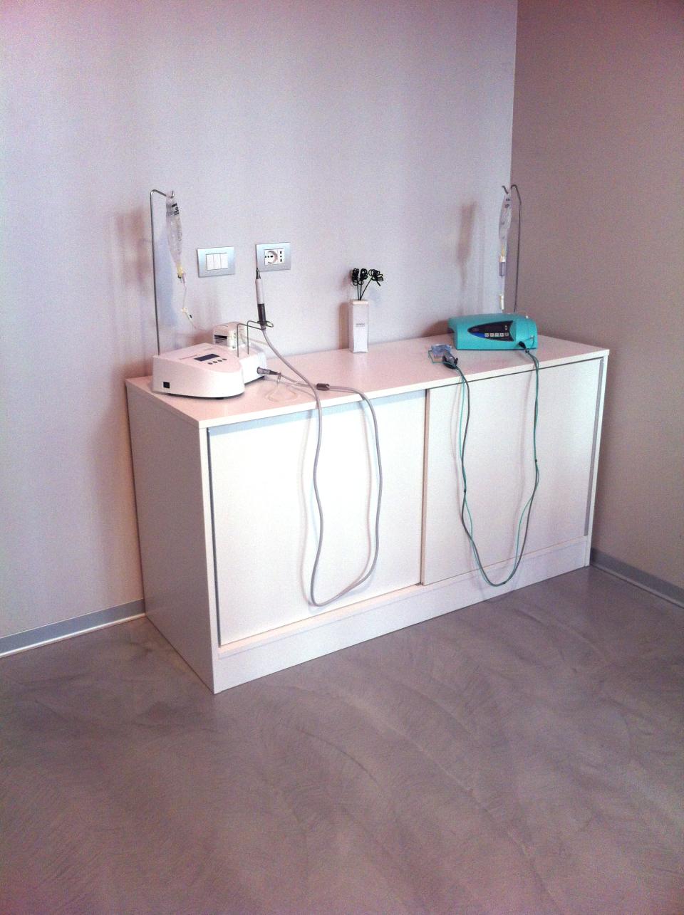 Apparecchiature mediche su un mobile bianco contro una parete rosa chiaro. Bombola di ossigeno e tubi pendenti.