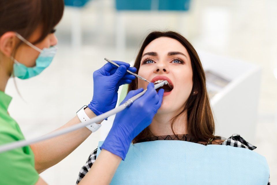 Dentista esamina i denti del paziente con strumenti in uno studio dentistico. La bocca del paziente è aperta; il dentista indossa mascherina e guanti.
