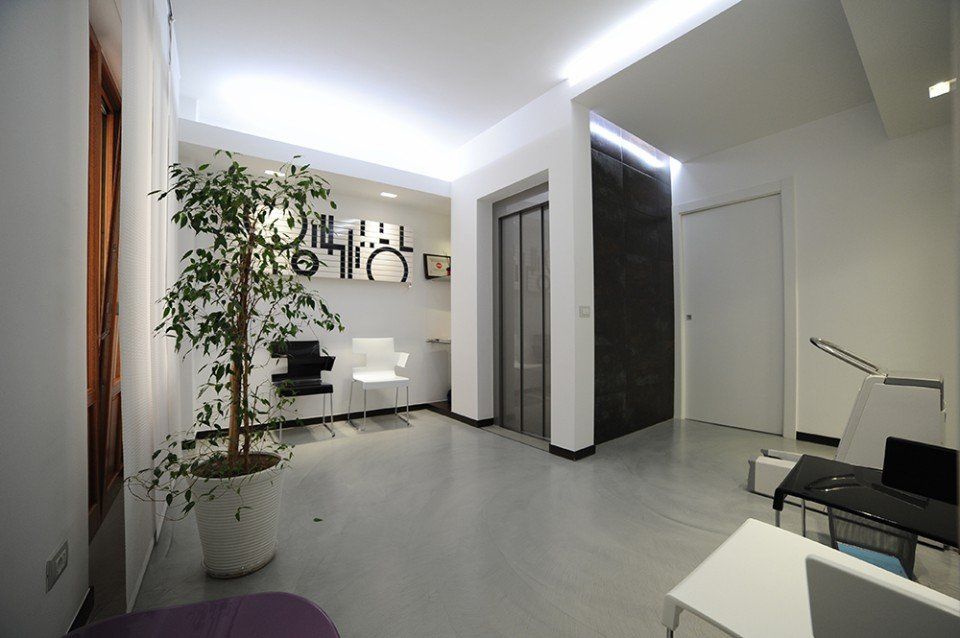 Interni moderni: hall con ascensore, opere d'arte, piante in vaso, pareti bianche, pavimento grigio e illuminazione da incasso.