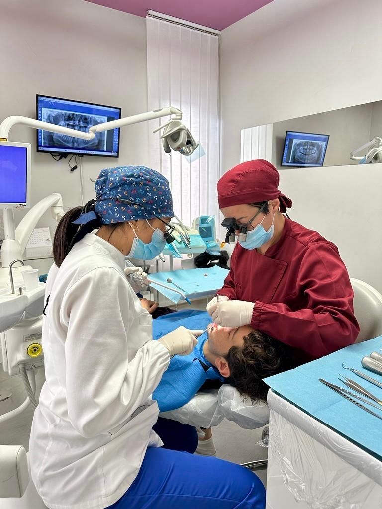 Un dentista e un assistente eseguono un intervento odontoiatrico su un paziente in una clinica, con gli strumenti visibili.