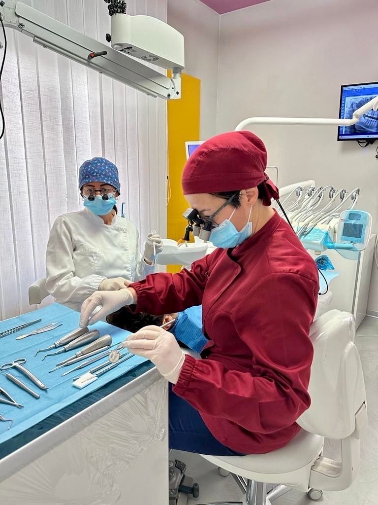 Due dentisti in divisa chirurgica; uno lavora su un paziente seduto sulla poltrona del dentista, l'altro lo assiste. Studio dentistico moderno.