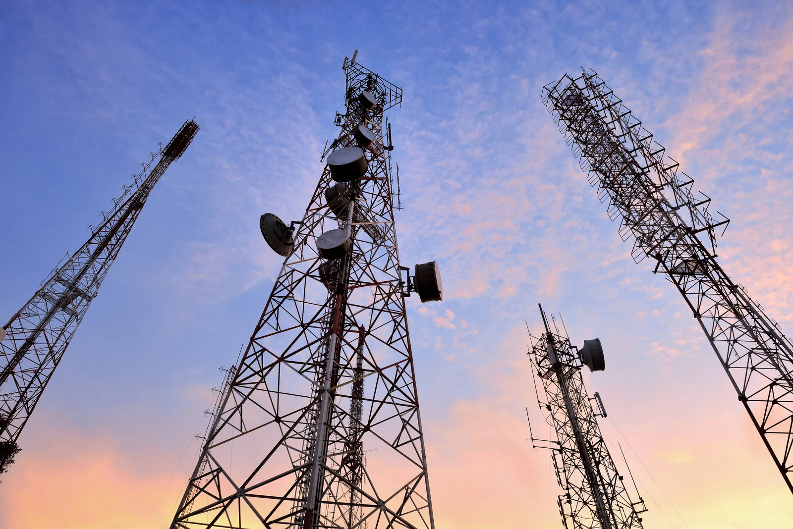 A group of telephone towers are silhouetted against a sunset sky.