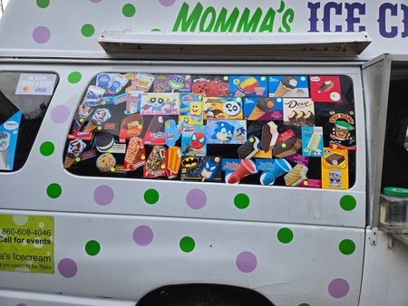 Side view of a white ice cream truck with purple and green polka dots, displaying a menu of treats on the side window.