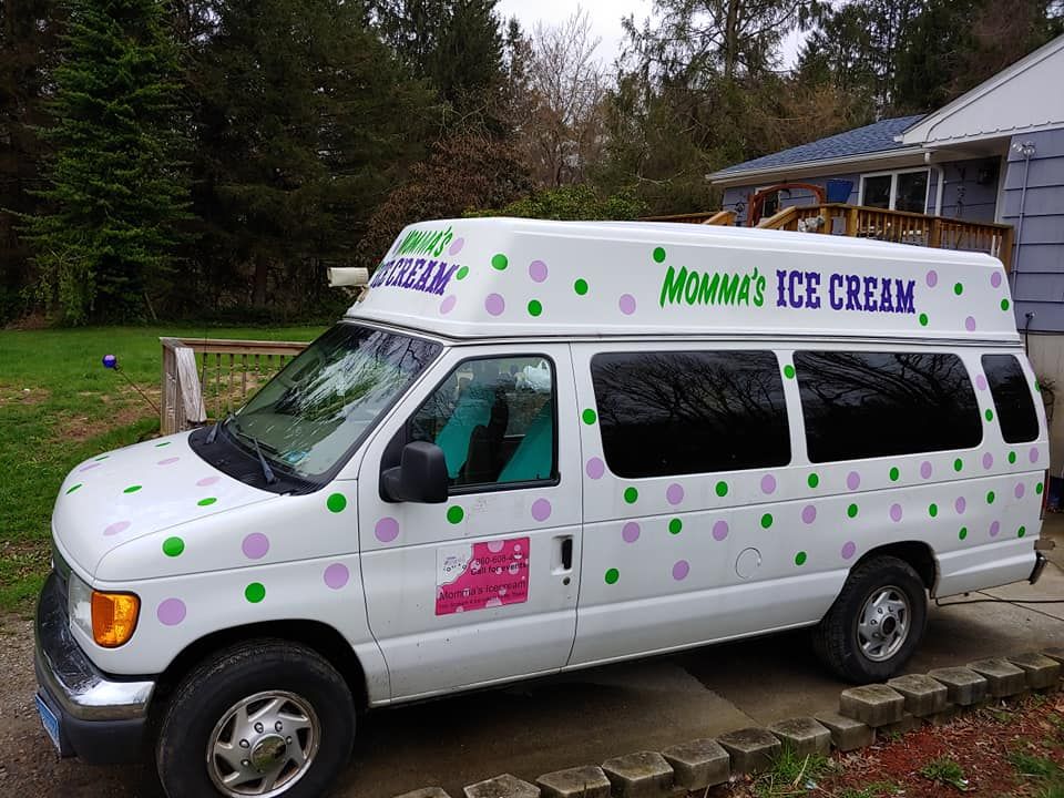 A white Momma's Ice Cream van parked on a driveway, covered in green and purple polka dots, with tinted side windows.