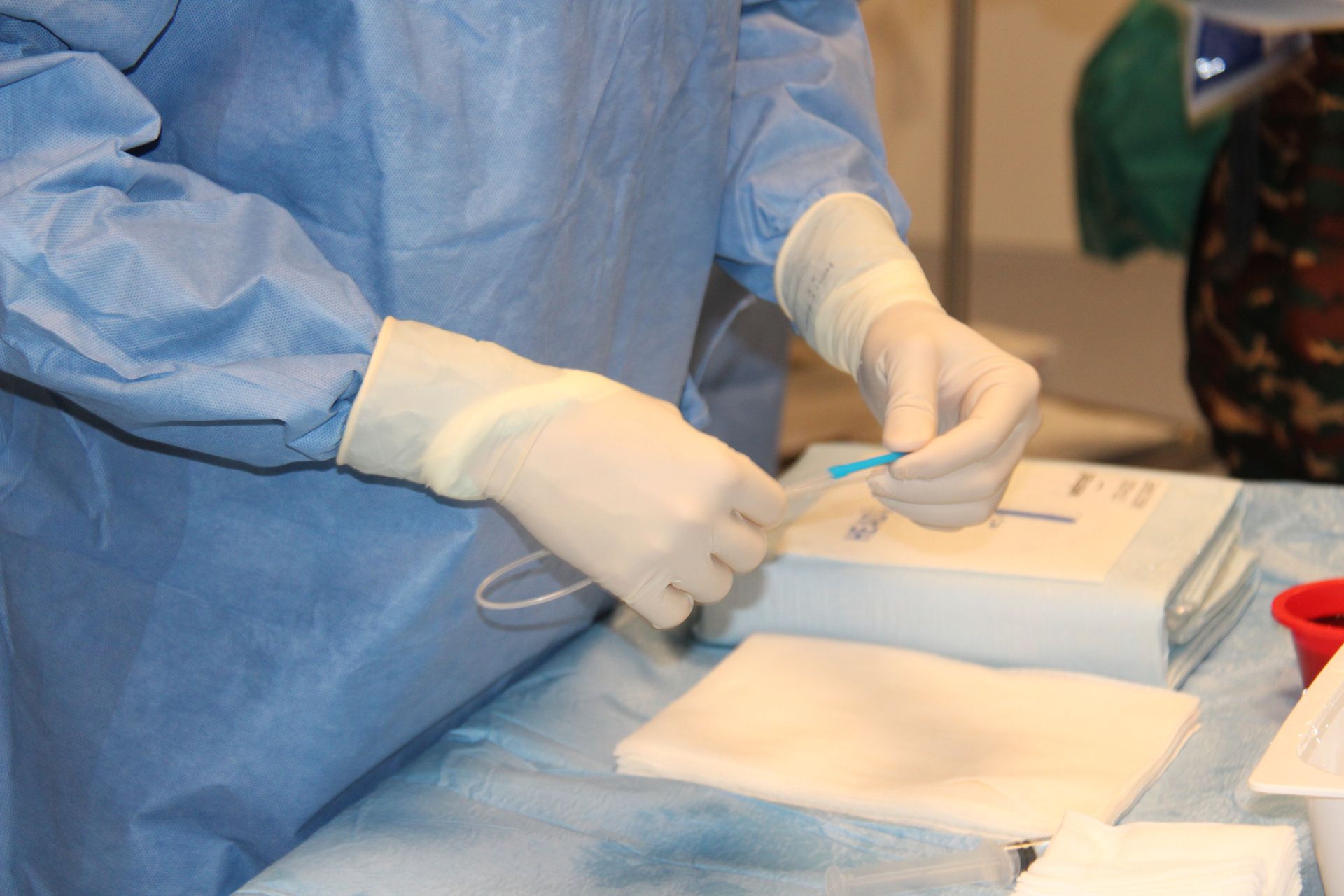 Person in surgical attire prepares medical equipment, holding a small blue tube with gloved hands.