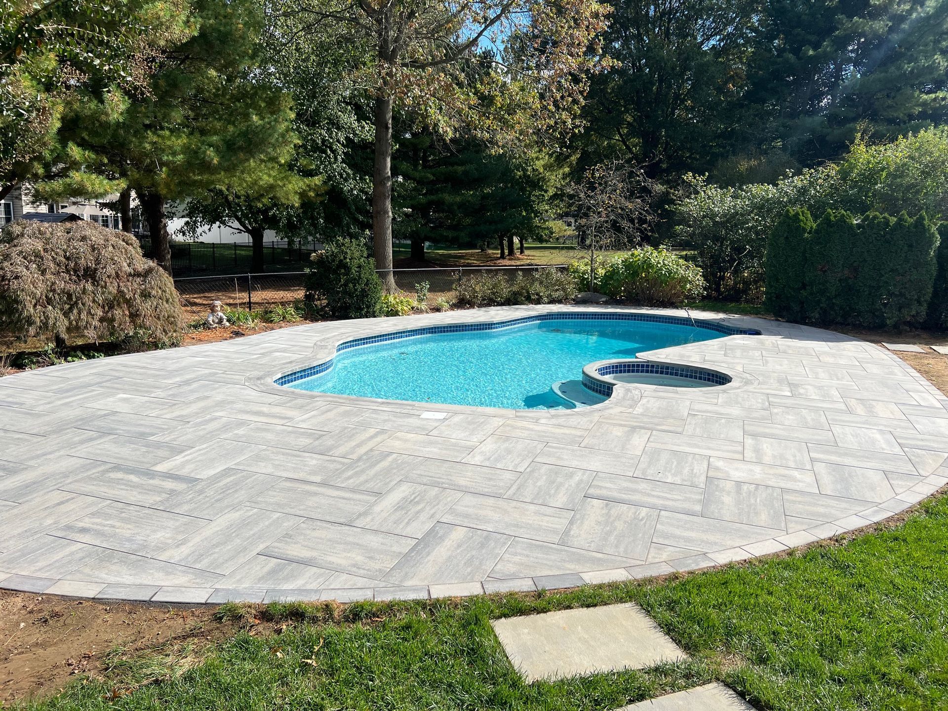 Backyard swimming pool with light gray patio pavers and surrounding trees and hedges