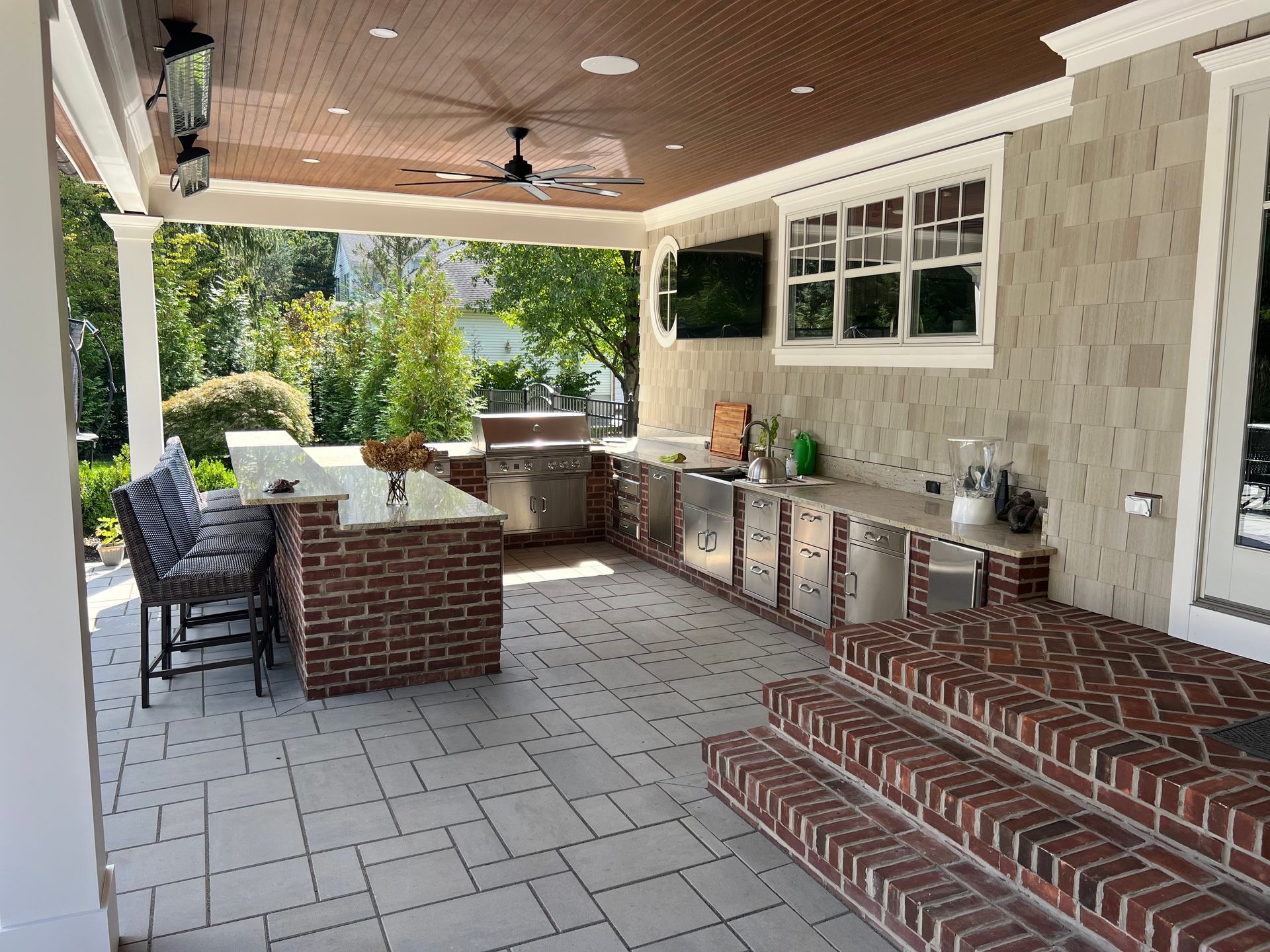 Outdoor kitchen with brick accents, stainless steel appliances, and stone flooring.