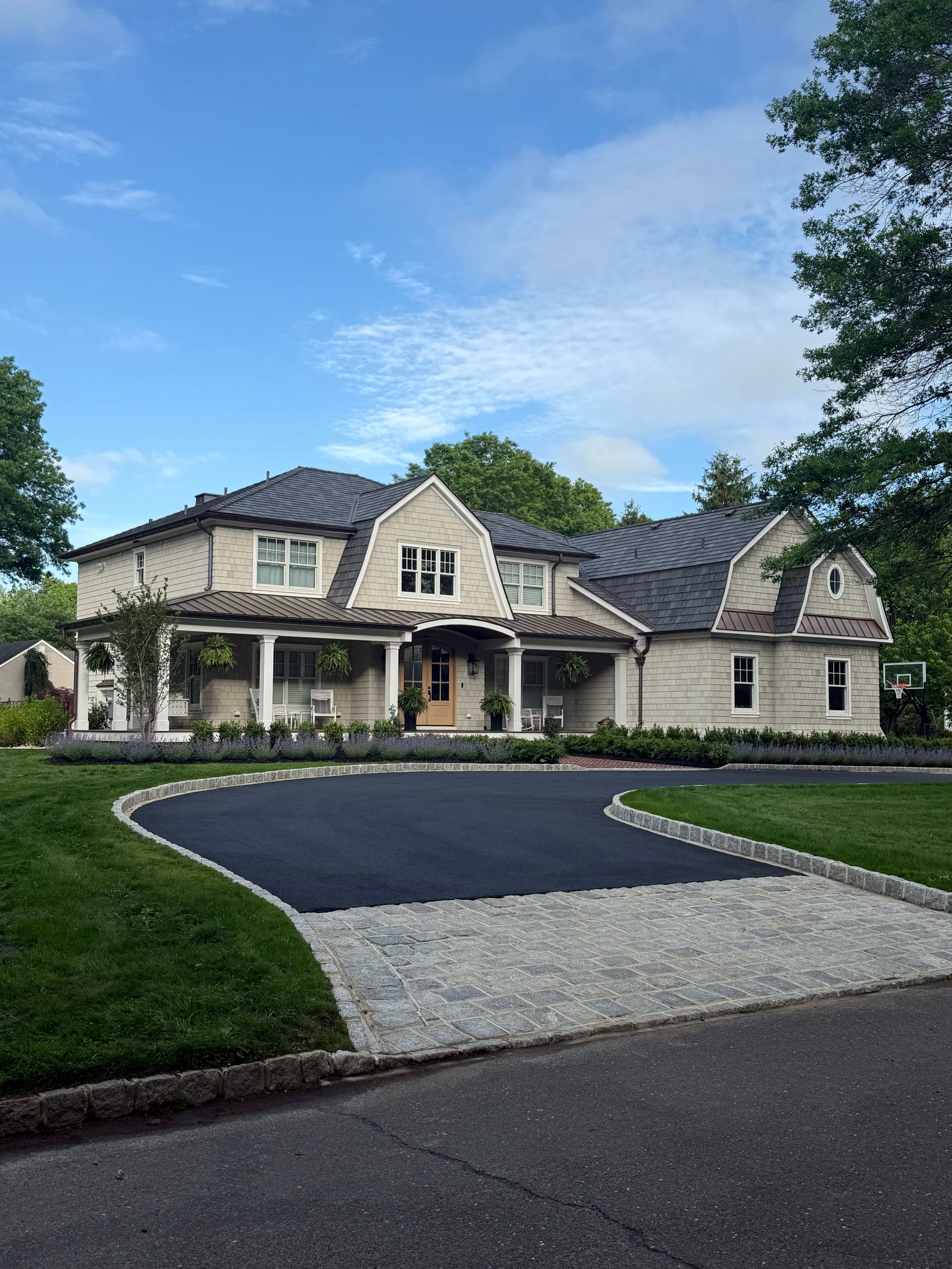 Large beige house with black roof, blue sky, green grass, and black paved driveway.