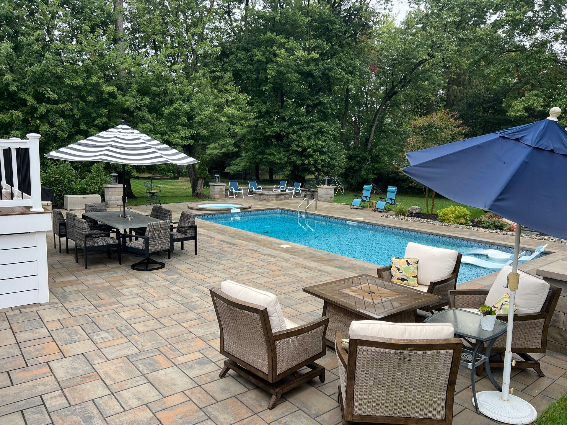 Patio with pool, seating areas, umbrellas, and lush green trees.