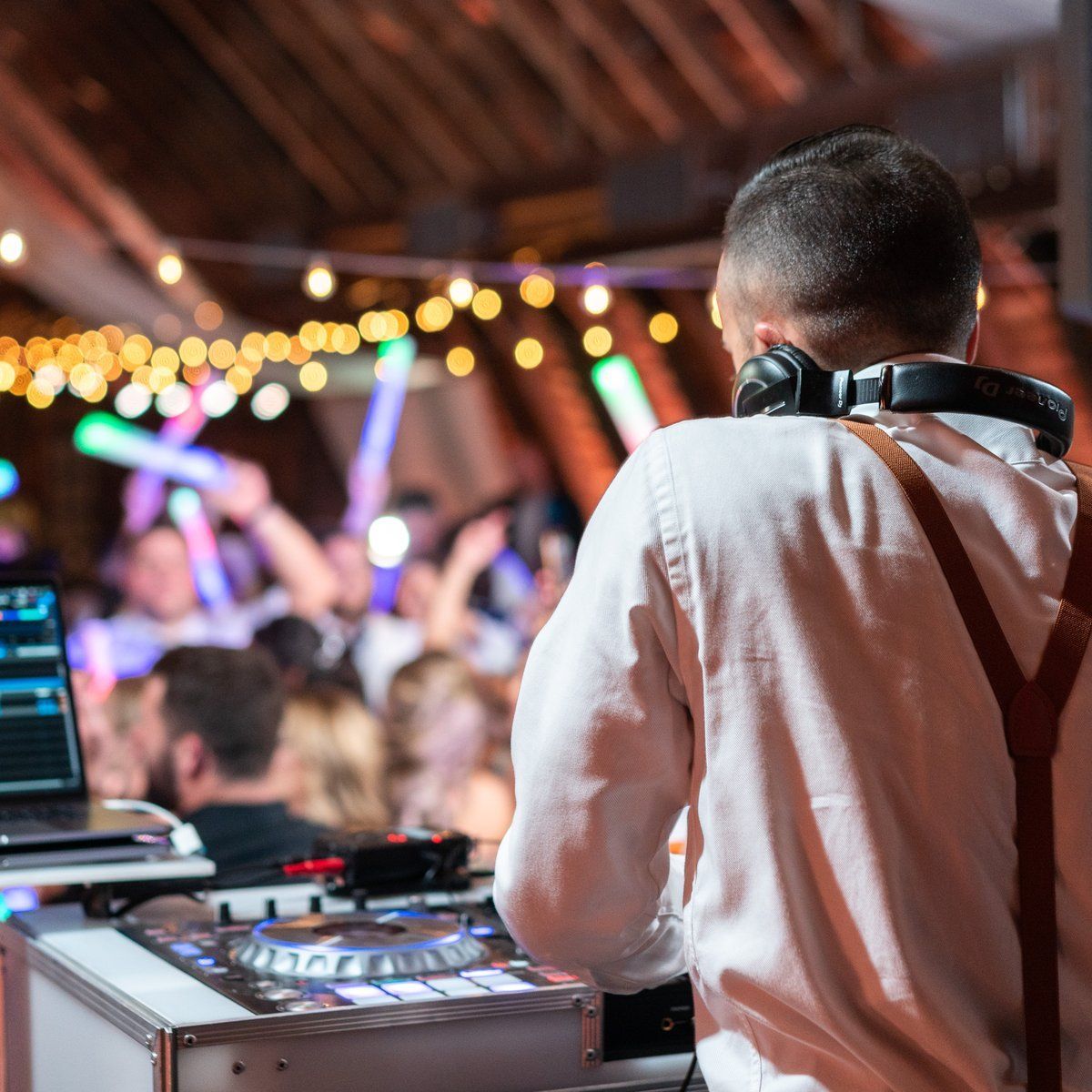 DJ mixing live over a packed dance floor with glow sticks