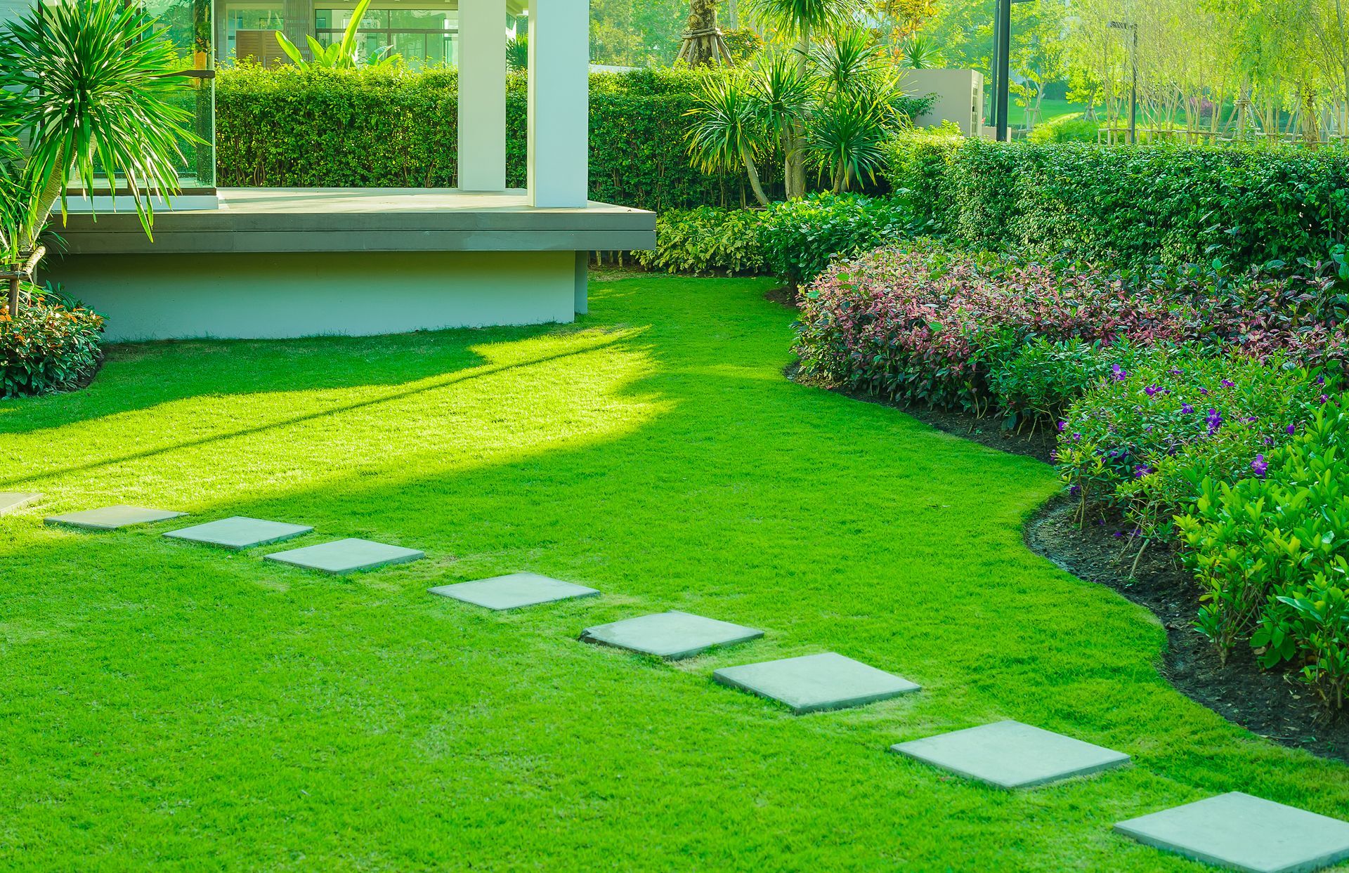 Curved stepping stone path across a lush green lawn with tropical plants and shrubs.