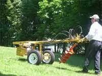 Man operating a yellow tiller on a grassy field.