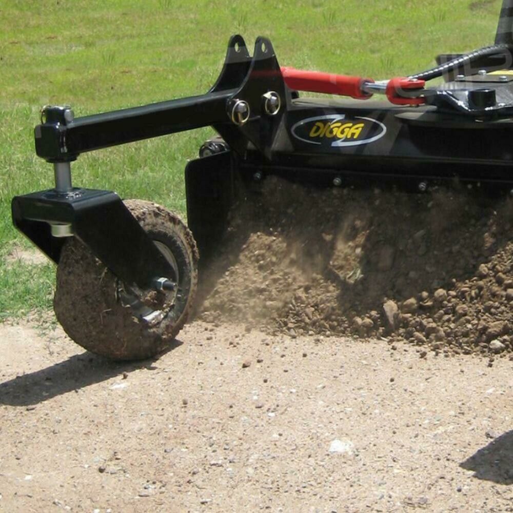 A tractor attachment tilling dirt with a rotating blade, wheel for stability, on a gravel road.