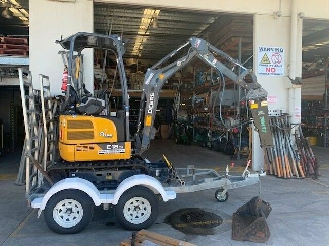 Yellow and grey excavator on a trailer in front of a workshop.