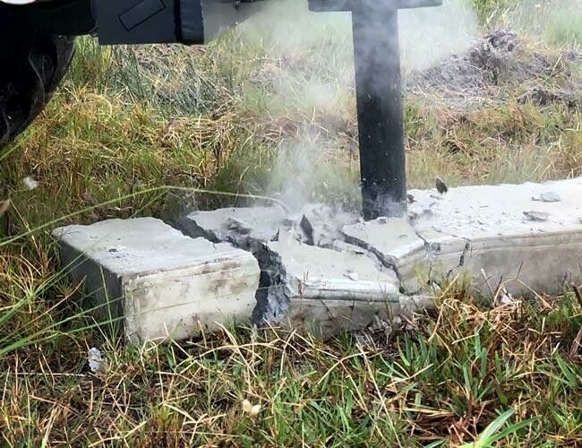 A jackhammer breaks apart a concrete base outdoors, with dust rising.