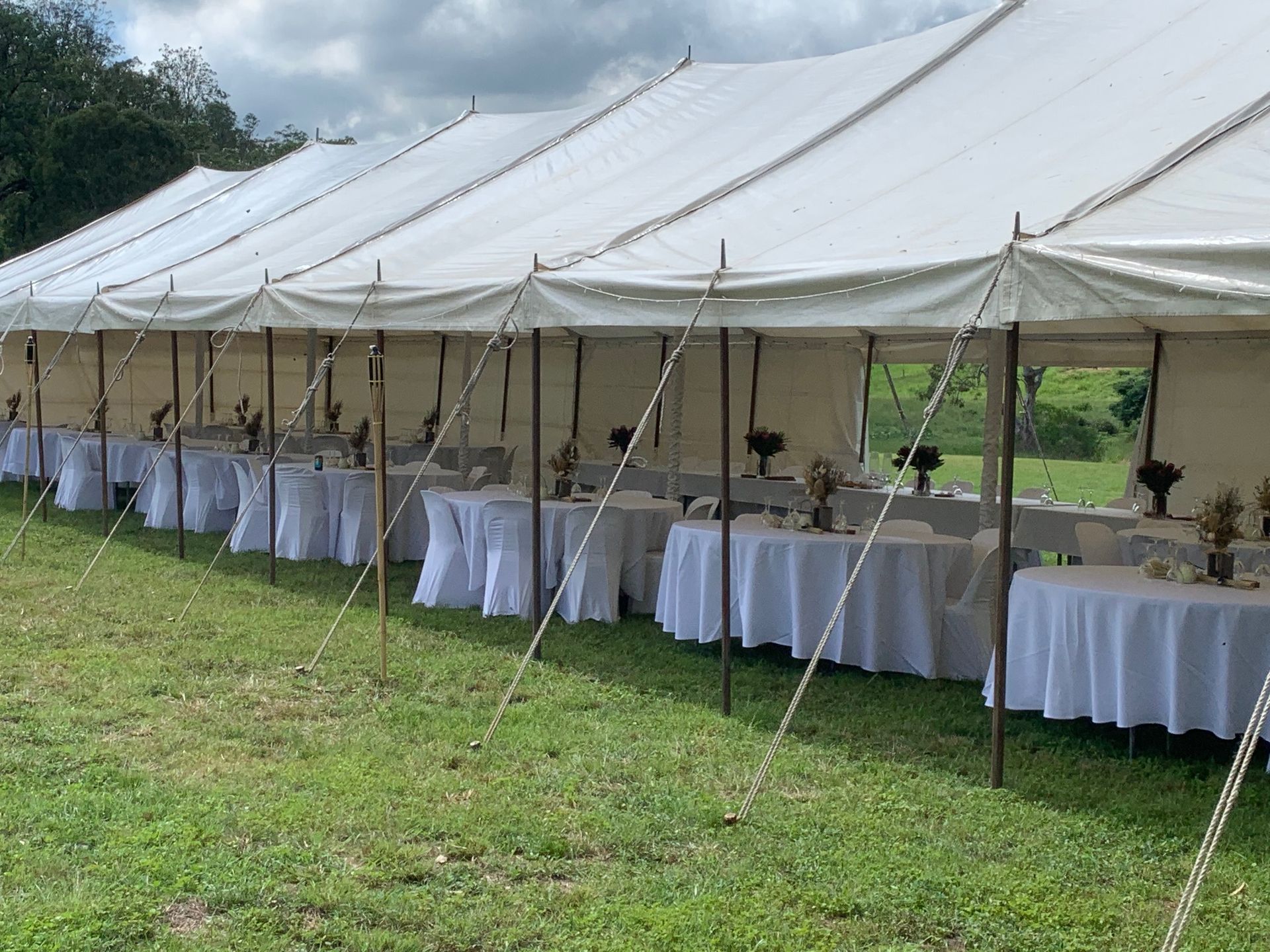A Row Of White Tables And Chairs Under A Tent In A Field – Caboolture, QLD - R & R Hire Services