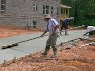 Construction workers smoothing wet concrete with long handled tools at a building site.
