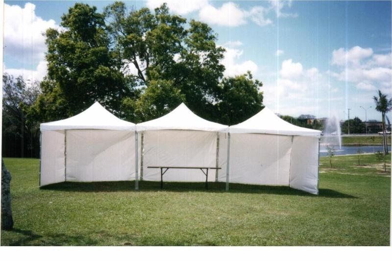 White outdoor tent with a bench inside on a grassy lawn, with trees and a pond in the background.