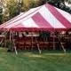 Pink and white striped party tent set up on green grass, with tables and chairs inside.