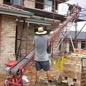 Construction worker using a conveyor belt to move bricks at a building site.