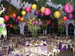 Indoor event with decorated tables, chairs, hanging lanterns, and flower arrangements.