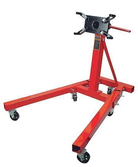 Red engine stand with a black mounting plate and wheels, for supporting an engine during repair.
