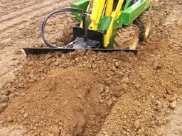Yellow and green trencher digging a trench in brown soil.