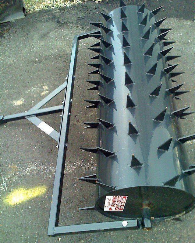Black lawn aerator with spikes, metal frame, and tow hitch, on asphalt.