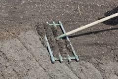 A person using a garden rake to smooth soil in a garden bed.