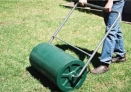 Person rolling a green lawn roller on grass.